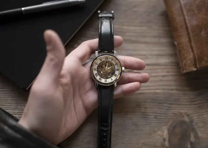 ¿Por qué invertir en un reloj vintage? Reloj vintage con correa de cuero negro y mecanismo visible en una mano.